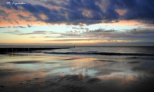 Krajobraz plaży oraz wzburzonego morza podczas zachodu słońca.