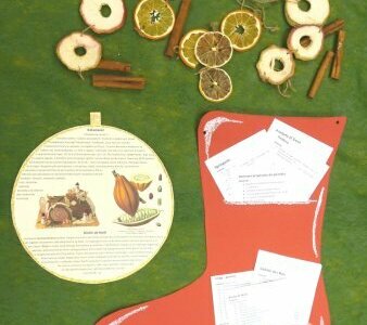 Board in the shape of a bauble with information about Christmas treats. Next to a red sock with recipes and various Christmas spices. 