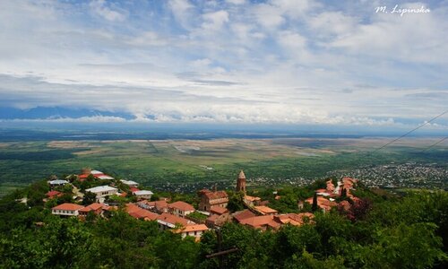 Landscape depicting a town, with mountains and fields in the distance.