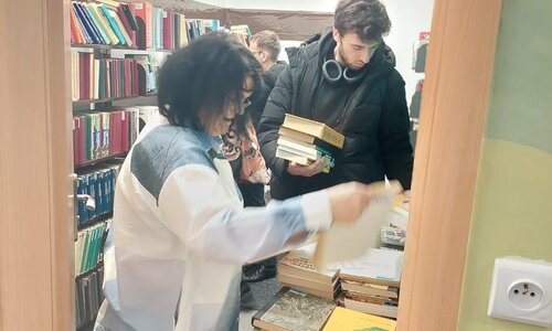 Uczestnicy akcji "Przygarnij książkę! przeglądający książki na stolikach.